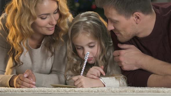 Parents Helping Daughter Write Letter to Santa Claus, Smiling Into Camera, X-Mas alt