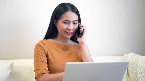 Young woman sitting on sofa using laptop and smart phone for work at home