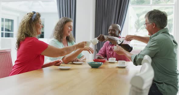 Animation of happy diverse female and male senior friends drinking coffee at home alt