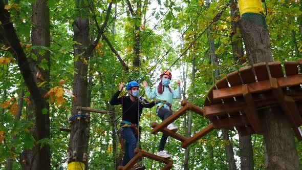 Little girl and instructor in medical masks and safety equipment engaged climbing rope park. 