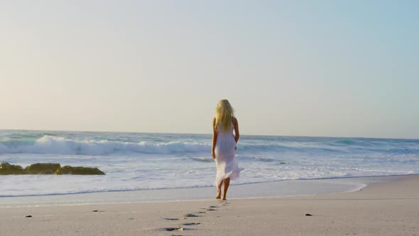 Woman walking towards sea on beach during sunset