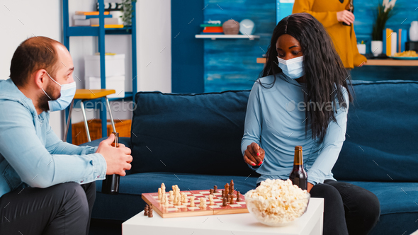 Cheerful man playing chess with african friend wearing face mask