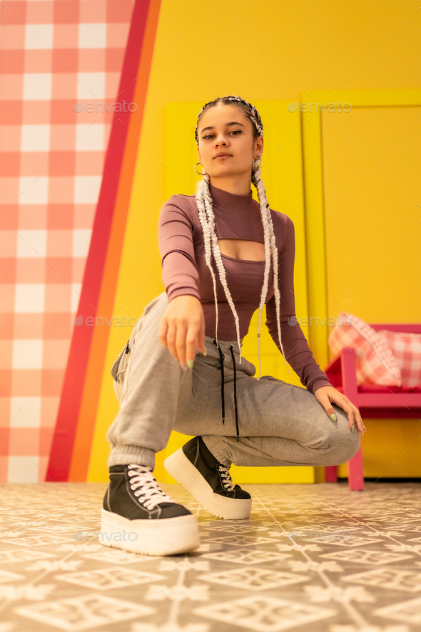 Girl with white braids on a yellow background, crouching in an alternative girl pose