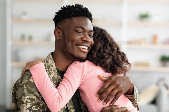 Side view of black man in military uniform hugging child