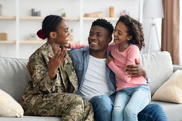 Cheerful family sitting on couch, mother soldier back from service