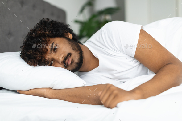 Sad indian guy in pajamas laying in bed