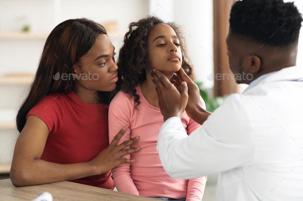 African american doctor palpating school girl throat at clinic