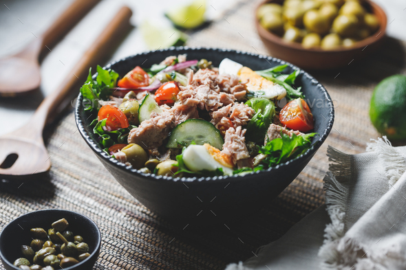 Canned tuna salad with fresh vegetables, capers and olives in a black bowl. - Stock Photo - Images