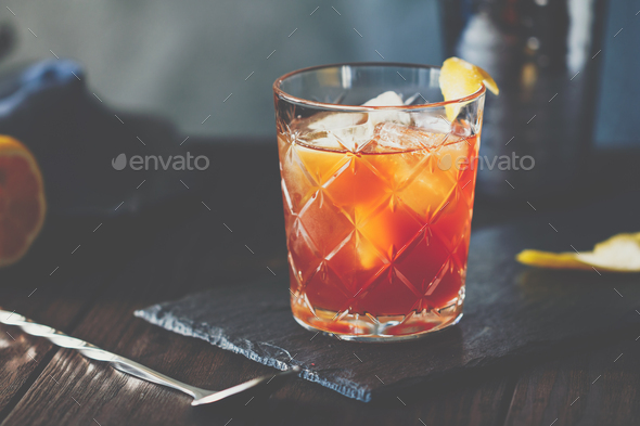 Orange or red coctail in an old fahion glass with citrus and ice cubes on a bartender table - Stock Photo - Images