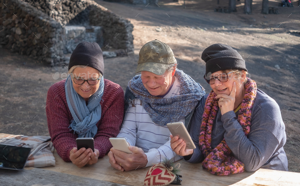 Group of smiling mature seniors people looking at mobile phone. Sitting at a wooden table