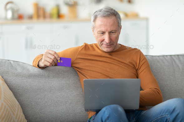 Casual mature man using pc and credit card at home