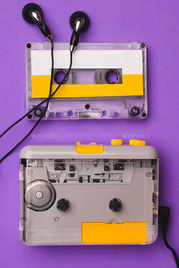 Cassette player with earphones and cassette tape on purple background. Stock Photo by