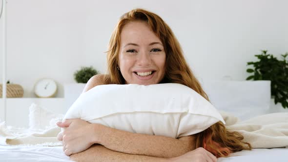 girl woke up in  good mood lying on bed laughing and cuddling up to pillow.
