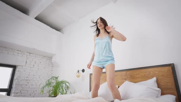 Happy Young Slim Woman Jumping on Bed in Slow Motion and Falling Down Smiling alt