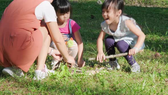 Mother and two daughters collecting firewood and kindling bonfire at camping place in forest. alt