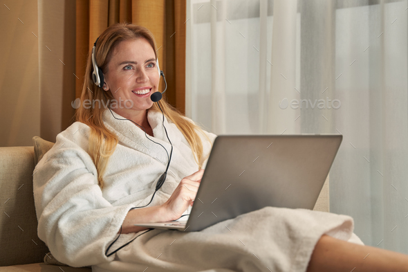 Positive woman talking into headset while lying with laptop
