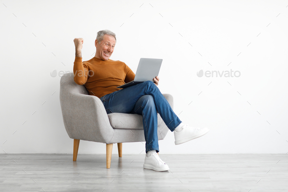 Mature man using laptop celebrating success shaking fists