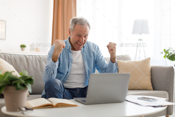 Mature man using laptop celebrating success shaking fists screaming yes
