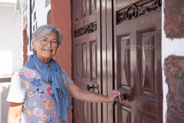 Smiling senior woman short hair opening a large wooden door of the country house when come back home