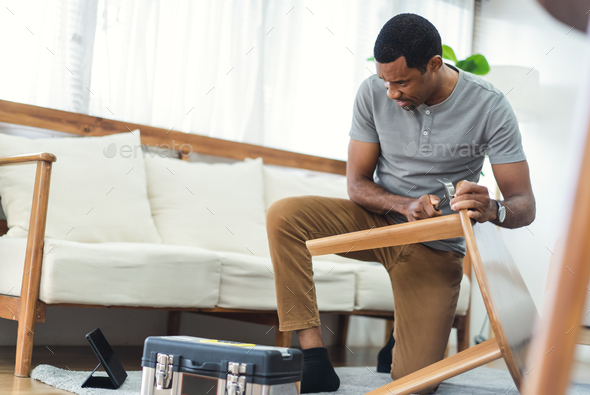 Happy black man watching online tutorial instructions for assembling furniture assembling at home