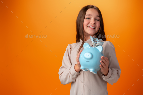 Teen girl with piggy bank on orange color background