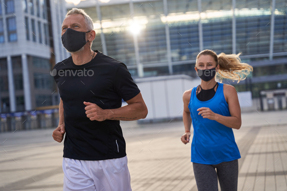 Active middle aged couple, man and woman wearing protective masks during morning run in urban