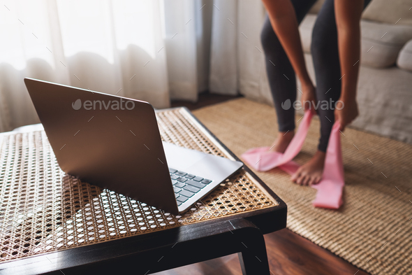 A woman with rubber resistance band and watching online workout tutorials on laptop at home