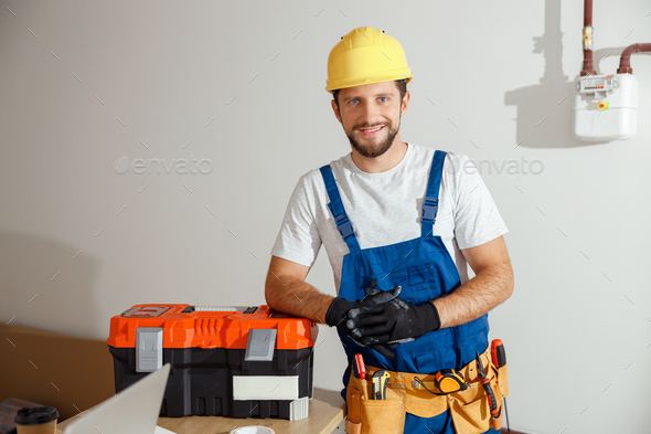 Cheerful electrician technician in uniform, hard hat and protective gloves smiling at camera while