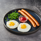 Classic breakfast of fried eggs, sausages and green peas on dish on gray background - PhotoDune Item for Sale