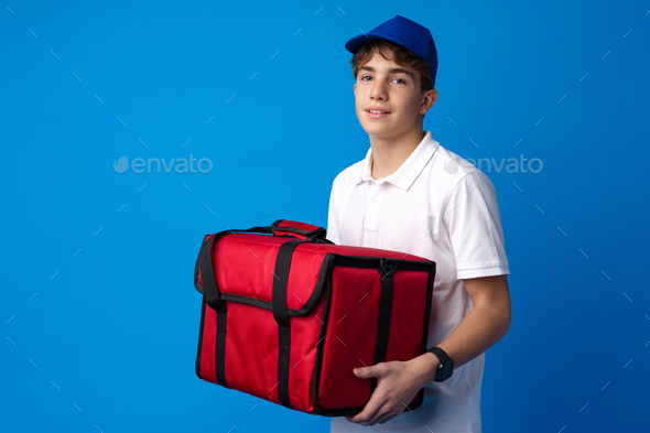 Portrait of pizza delivery boy with thermal bag against blue background
