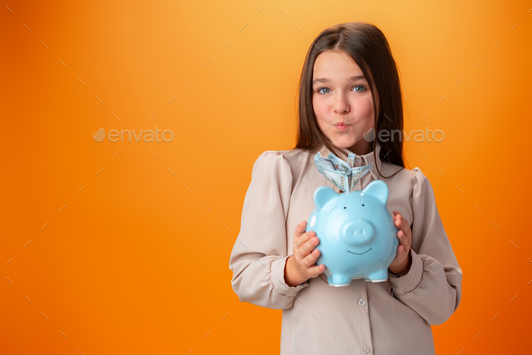 Teen girl with piggy bank on orange color background