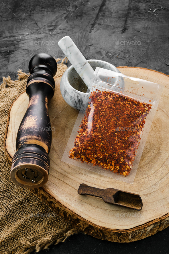 Wooden cross section with chili flakes in plastic package and mortar and mill