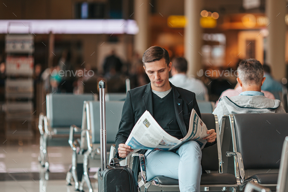 Passenger in an airport lounge waiting for flight aircraft. Young man with magazines in airport