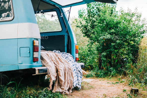 Blue-white retro van in nature, with cozy decorations, blanket and pillow