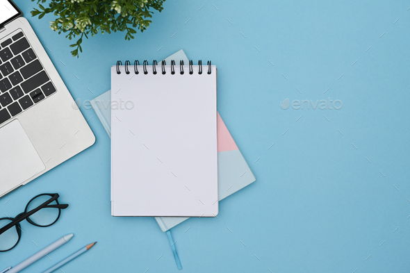 Empty notepad, eyeglasses and laptop computer on blue background. Top ...