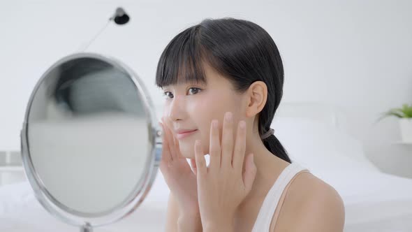 Beautiful face of young asian woman with happy smiling and touch cheek looking mirror. alt