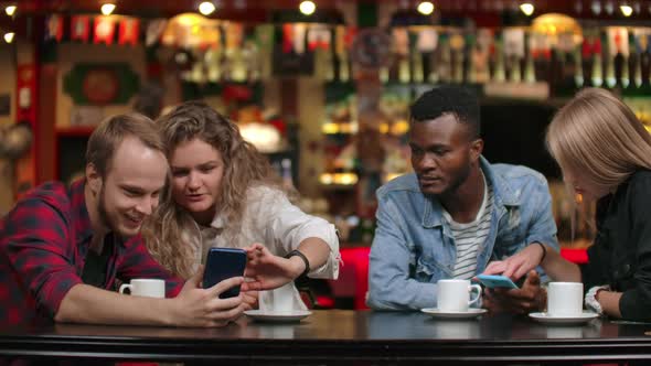 Multi-ethnic Couples Sitting in a Cafe Look at the Screens By Phone and Leaf Through Photos in the alt