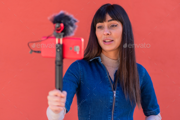 Brunette girl recording a vlog in a blue denim outfit. Red background ...