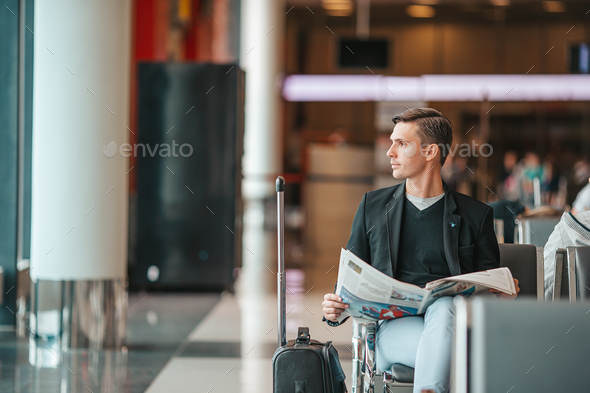 Passenger in an airport lounge waiting for flight aircraft. Young man with magazines in airport