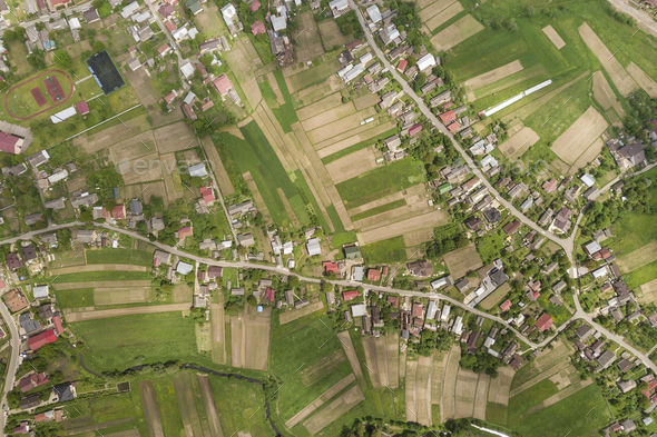 Top down aerial view of town or village with rows of buildings and curvy streets between green