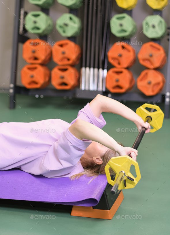 woman lying on training bench lifting barbell in gym, pushing exercise training chest
