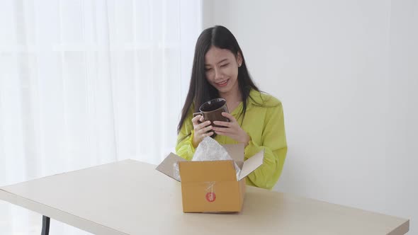 Young asian woman unpacking of parcel box with online shopping while satisfied at home. alt