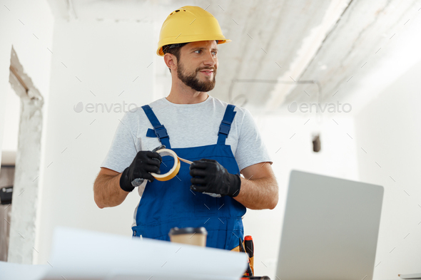 Confident handyman, electrician smiling aside holding duct tape for installing new electrical socket