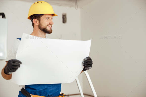 Portrait of thoughtful construction worker in hardhat looking away while studying blueprint