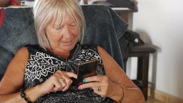 Senior Woman Looking on Mobile Phone Relaxing on Sofa at Home