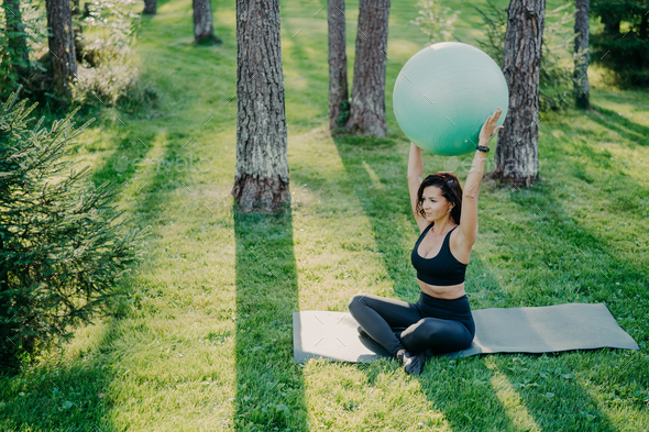 Fit sporty woman exercises with fitness ball sits on karemat in lotus pose