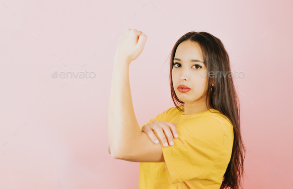 Young woman grabbing her arm muscle with strong attitude, woman power and feminism