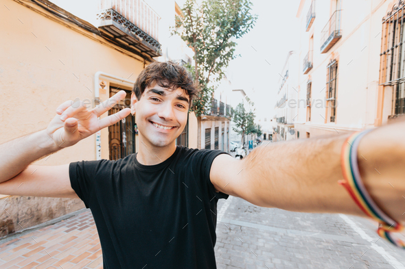 Happy young man wearing shirt taking a selfie in the city during a sunny day and smiling.