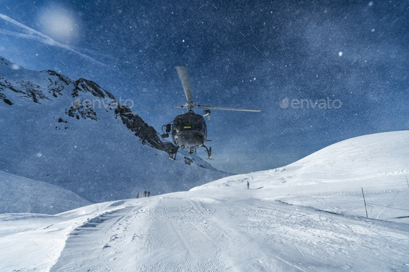 Mountain rescue team helicopter rescuing an injured skier after having a skiing accident in the Alps