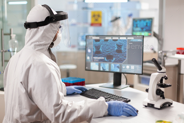 Medical scientist in ppe suit working with DNA scan image typing on pc